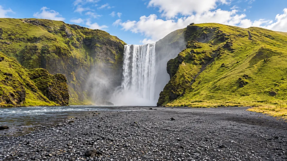 Skogafoss waterfall below green cliffs with plain foreground