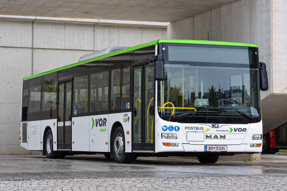 White-and-green MAN low-floor Postbus in VOR Regio colors with two side passenger doors at a covered Vienna stop.