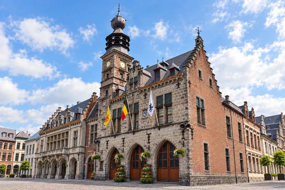 Binche town hall's stone front and brick clock tower with its dark tiered belfry dome.