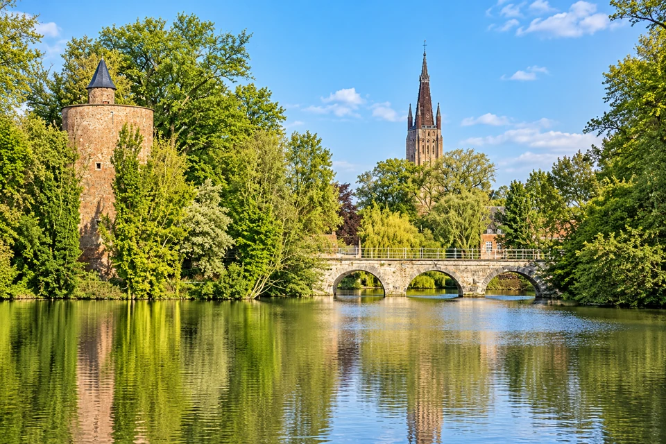Minnewater lake, a low three-arch bridge and the brick gunpowder tower in Bruges.
