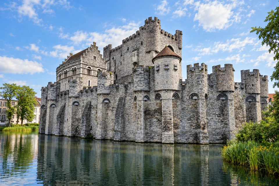 Gravensteen Castle's grey stone keep and projecting towers above the moat in Ghent.