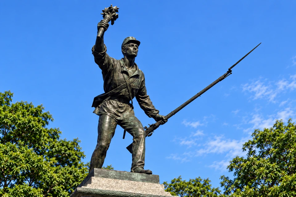 Detail of the bronze Juan Santamaria statue in Alajuela, with raised torch and angled rifle.