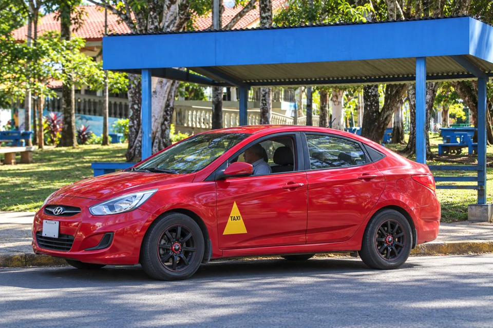 A compact red Costa Rican taxi with a yellow triangular permit marking on the front door.