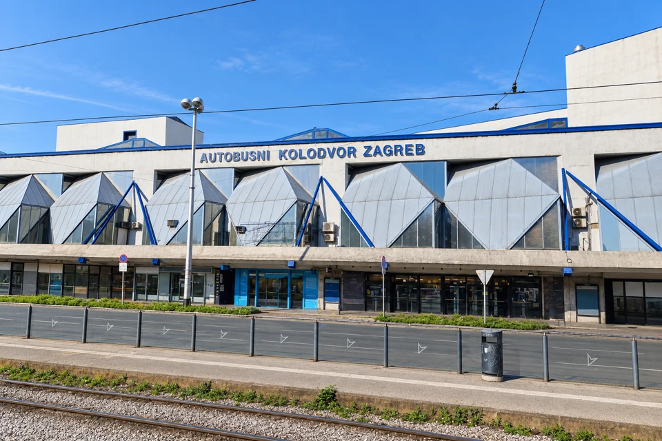 The angular blue-trimmed frontage of Autobusni Kolodvor Zagreb, with tram tracks in front.