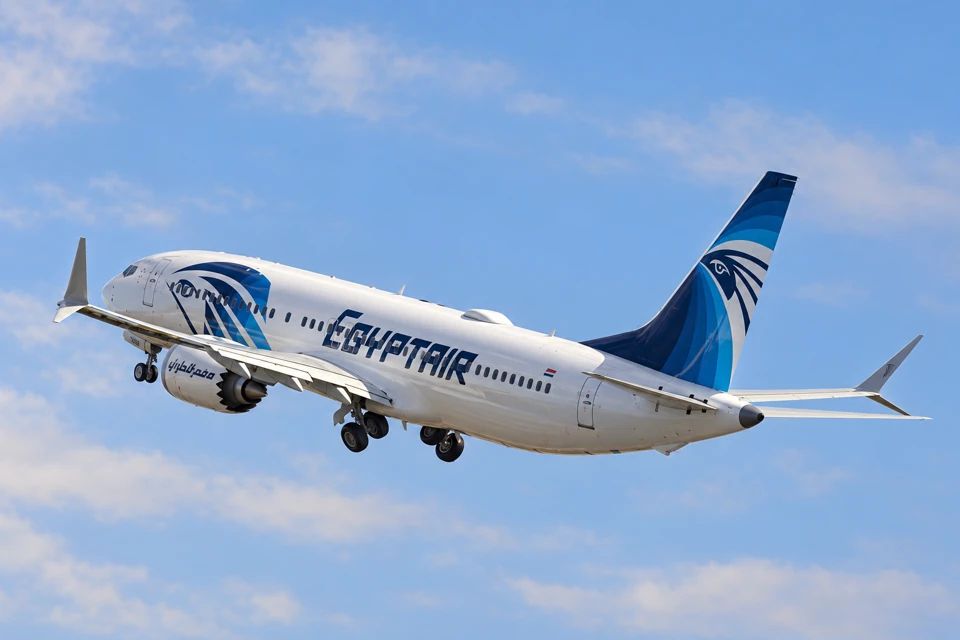 An EgyptAir Boeing 737 MAX 8 with blue Horus markings on the forward fuselage and tail, climbing with landing gear still visible.