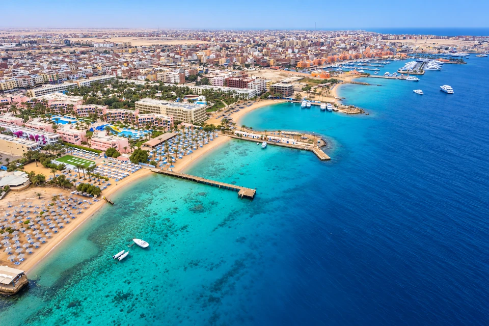 Hurghada's Red Sea waterfront with curved sandy bays, narrow piers, turquoise shallows and the dry city behind.