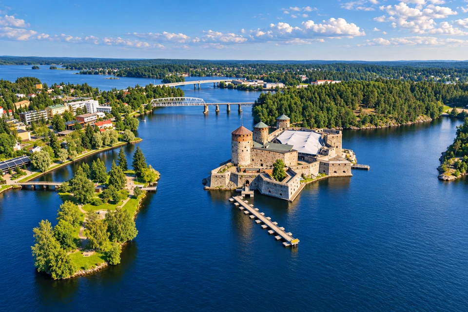 Olavinlinna Castle with round stone towers surrounded by blue water and green summer shores in Savonlinna.