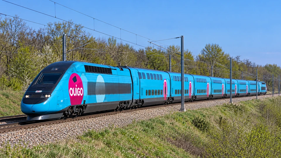 A turquoise OUIGO Grande Vitesse high-speed train with pink doors and double-deck passenger coaches.
