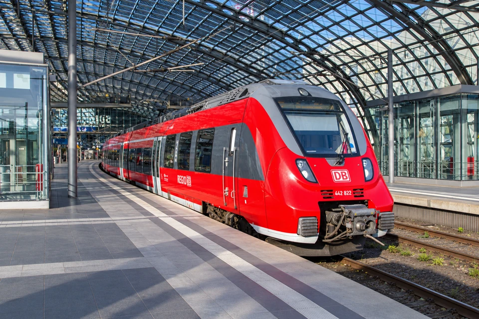 Red DB Regio Talent 2 regional train with a gray cab surround under Berlin Hauptbahnhof's curved glass roof.