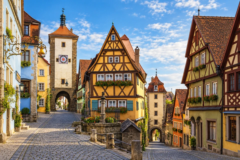 Rothenburg's Ploenlein street fork with a yellow half-timbered house between two medieval gate towers.