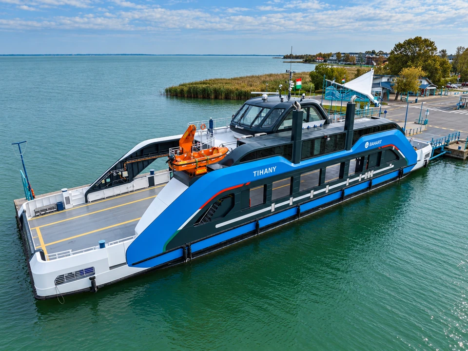Blue-and-white Tihany car ferry moored beside the turquoise-railed landing, with an empty vehicle deck.