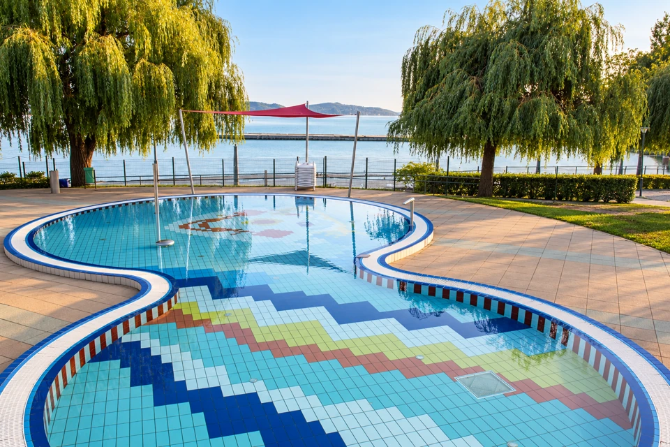 Esterhazy Strand's curving tiled outdoor pool beneath willow trees beside Lake Balaton in Balatonfured.