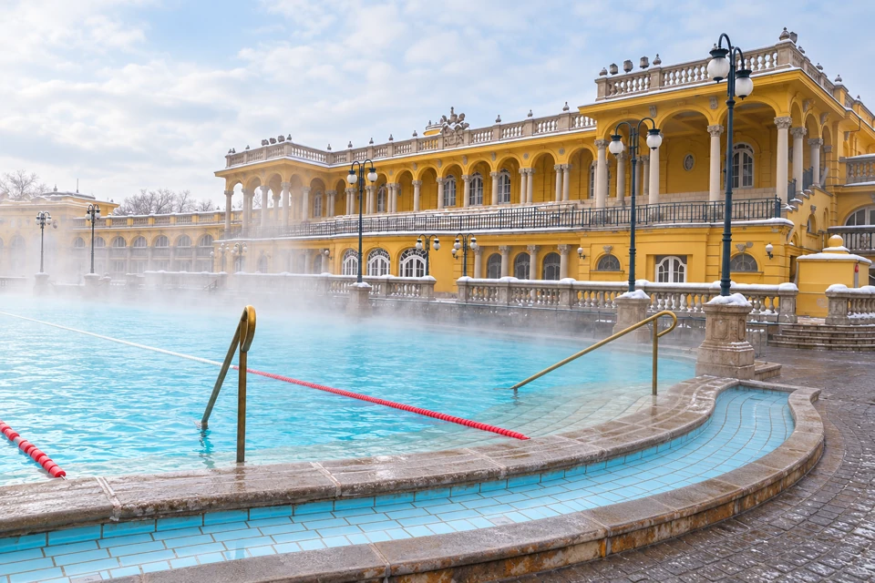 Steam above an empty outdoor pool at Budapest's Szechenyi Baths, with its yellow colonnades and lightly snowy balustrades.