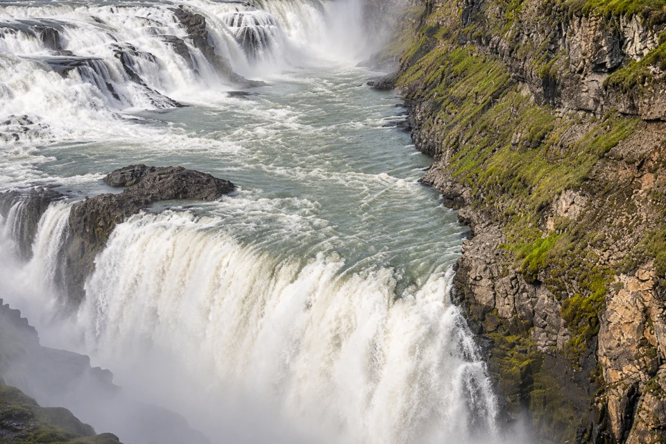 A close view of Gullfoss's lower drop plunging beside its rocky canyon wall, with upper cascades behind.