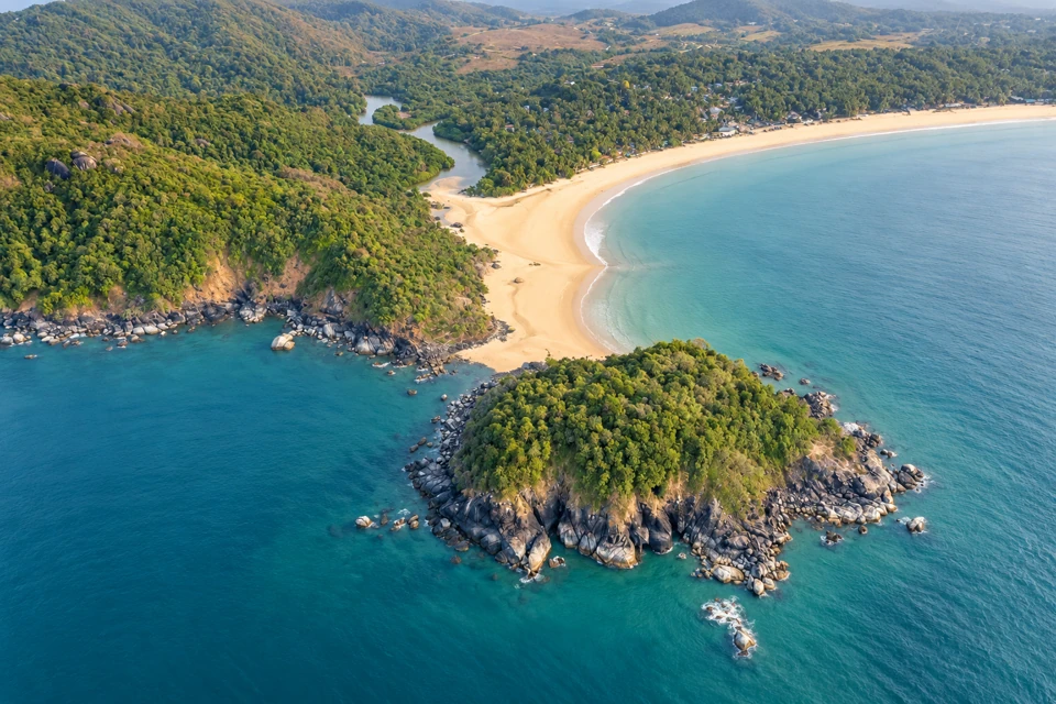 Palolem Bay in Goa, with its wooded rocky island, curving beach and palm-lined shore.