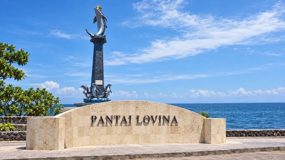 Lovina's dolphin monument above the curved Pantai Lovina stone sign.