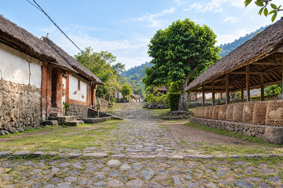 A worn stone lane between whitewashed thatched houses and an open communal pavilion in Tenganan Pegringsingan, Bali.