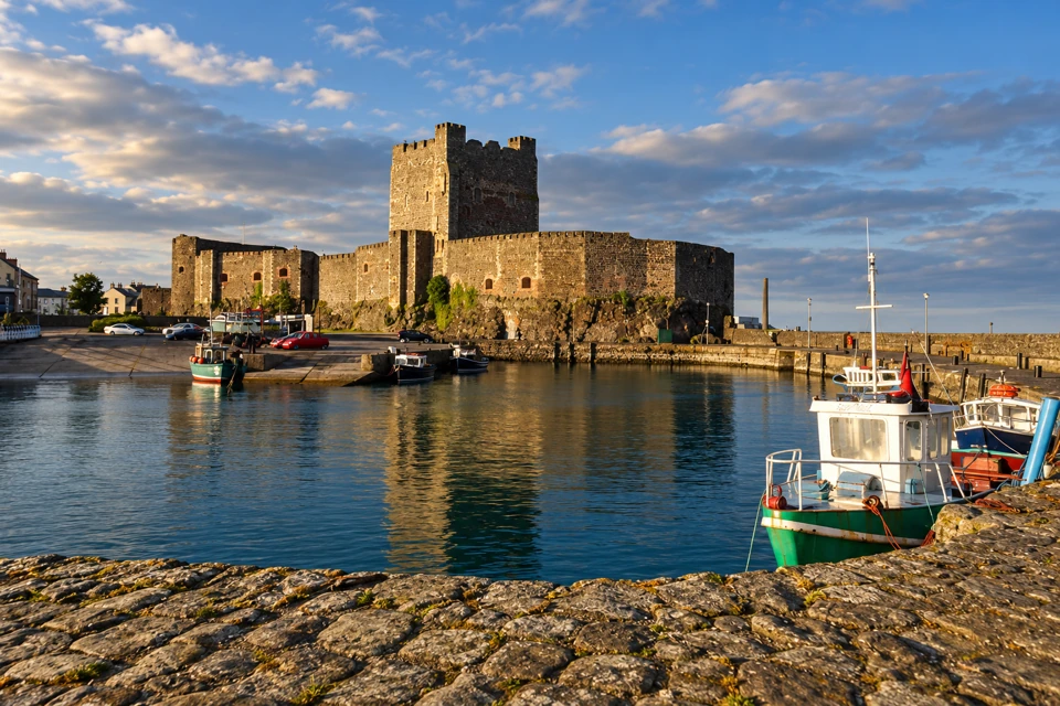 Carrickfergus Castle's square keep and curtain walls beside fishing boats in the harbour.