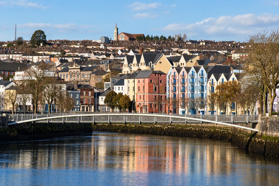 Shandon Bridge over the River Lee in Cork, with pastel gabled quayside buildings and a hillside of rooftops behind.