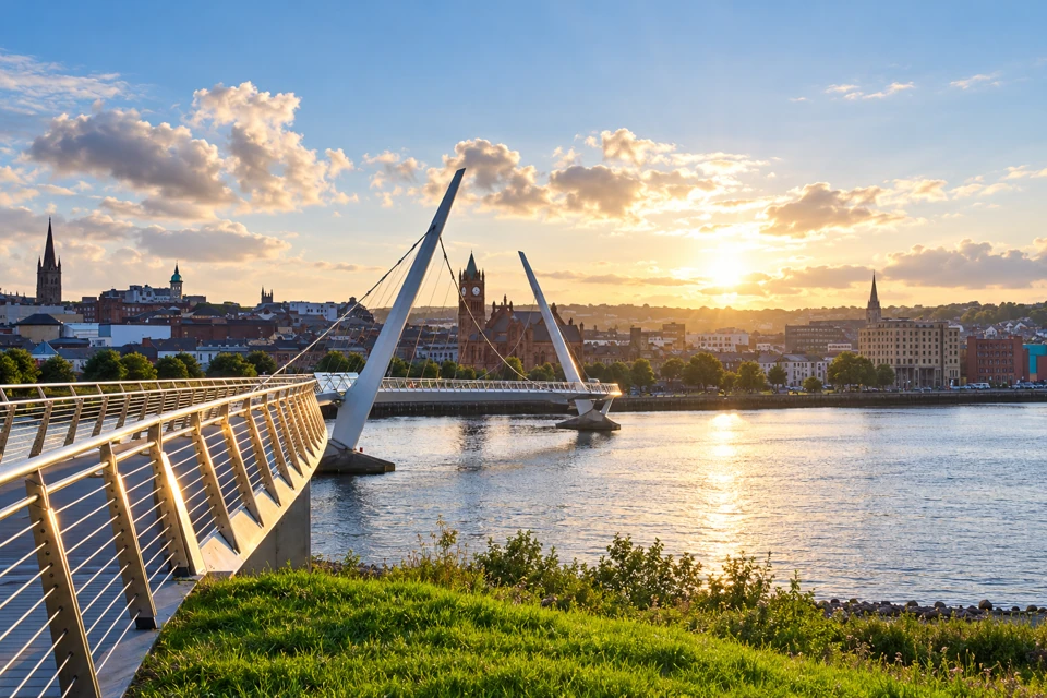 Derry's Peace Bridge curves over the River Foyle toward the Guildhall, with two oppositely leaning white pylons.