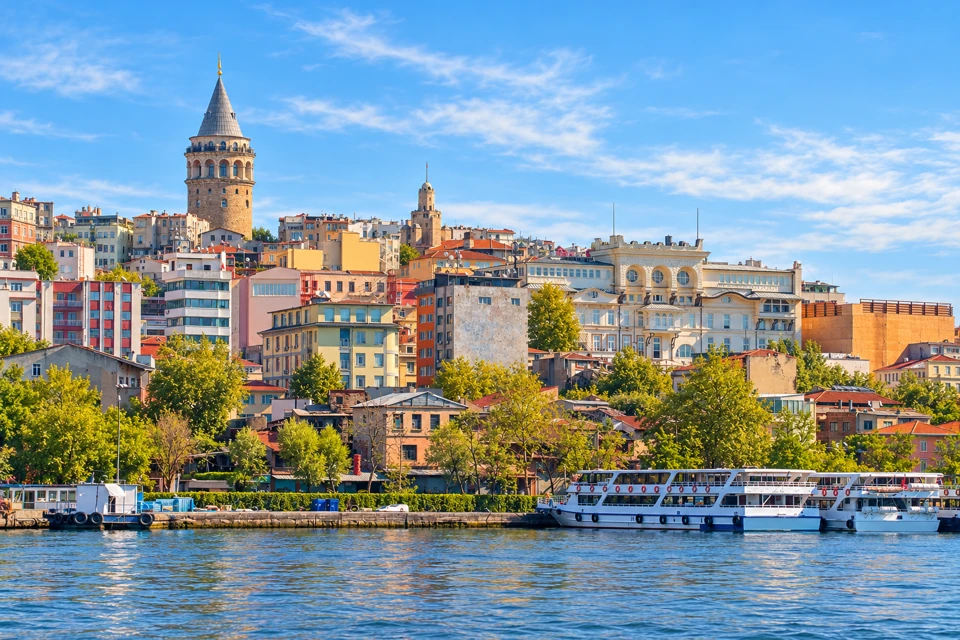 Galata Tower's stone shaft and conical roof above Karakoy's buildings and the Golden Horn waterfront in Istanbul.
