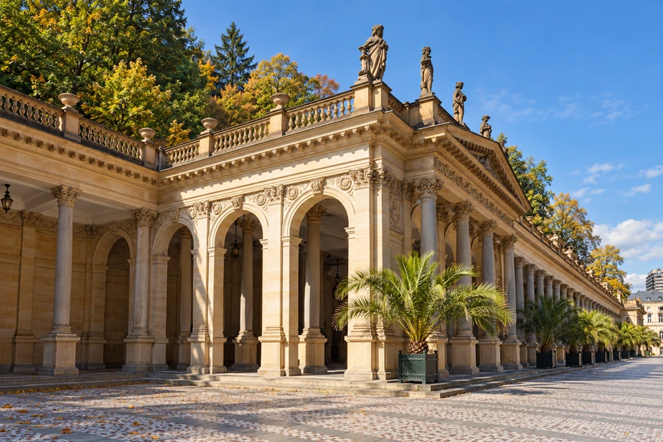 The long stone arcade and rooftop statues of Karlovy Vary's Mill Colonnade.