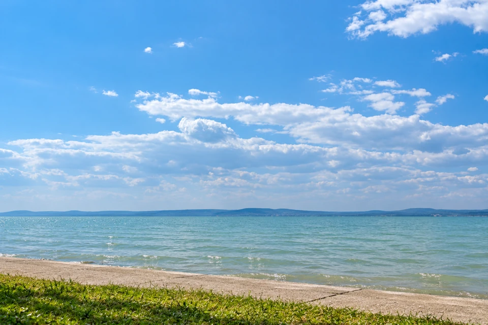 Blue-green Lake Balaton water beside a grassy lakeshore with low hills across the horizon.