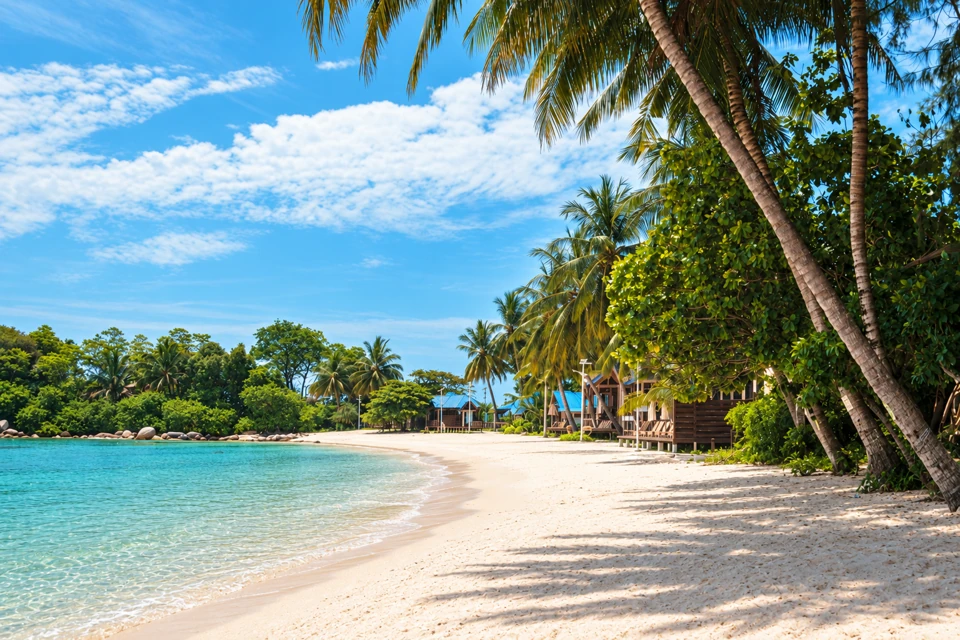 Teluk Pauh on Perhentian Besar with pale sand, shallow bay and palms beside timber lodges.