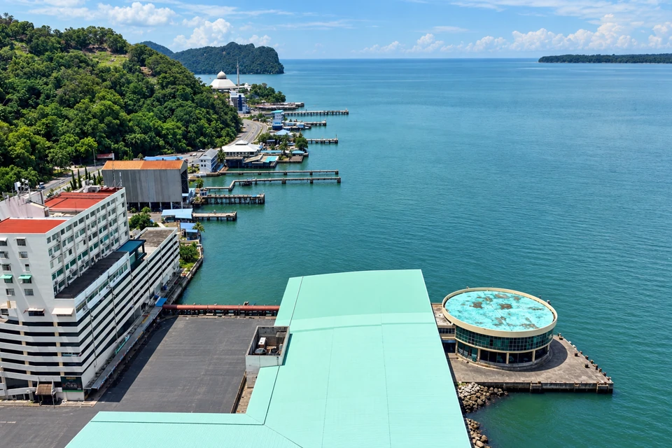 Sandakan waterfront in eastern Sabah, with market roofs, jetties and a forested headland beside the bay.