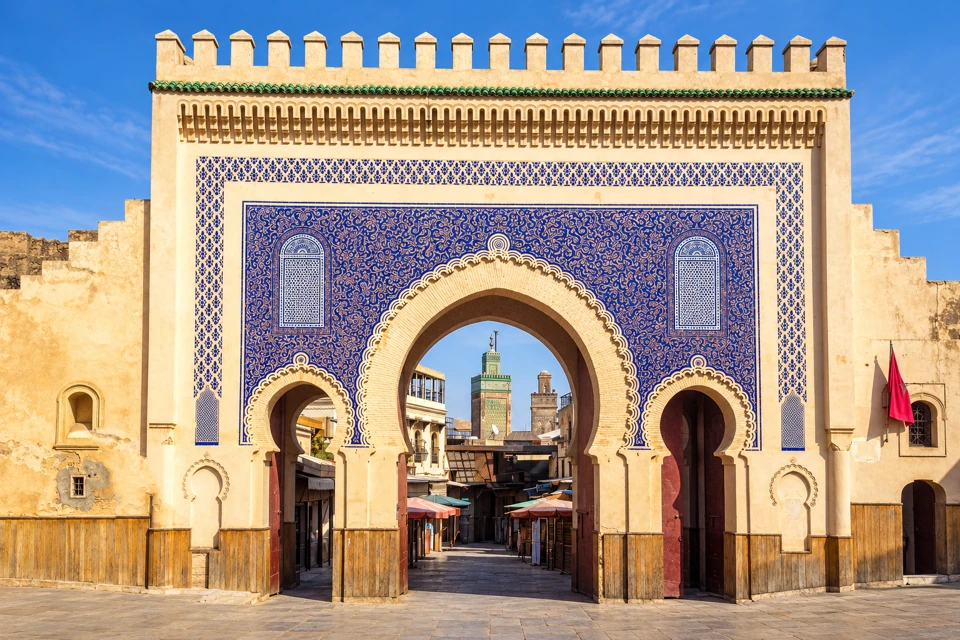The blue-and-cream outer face of Bab Bou Jeloud in Fes, with three arches and minarets visible beyond.