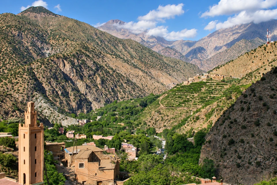 Terraced slopes, ochre village buildings and a green river corridor in Morocco's Ourika Valley.