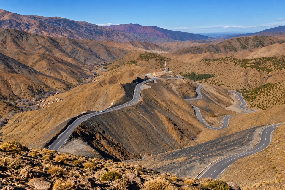 The paved Tizi n'Tichka road winds in hairpin bends across sparse ochre and dark rocky slopes in Morocco's High Atlas.