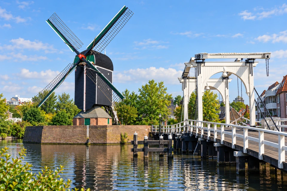 Black wooden De Put post mill with four lattice sails beside the white Rembrandtbrug in Leiden.