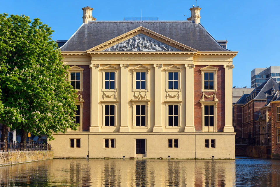 The cream pilasters and red-brick facade of the Mauritshuis reflected in Hofvijver water in The Hague.