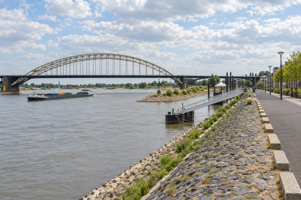 The Waalbrug's broad steel arch spanning the Waal beside Nijmegen's stone-lined Waalkade waterfront.