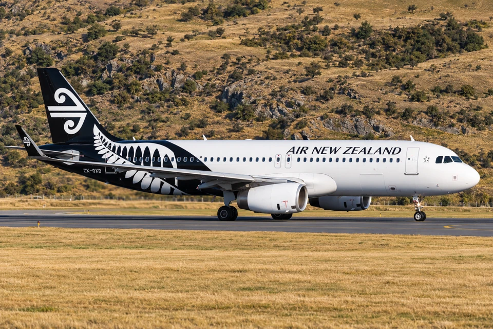 An Air New Zealand Airbus A320 with a white forward fuselage, black fern rear and koru tail on a Queenstown taxiway.