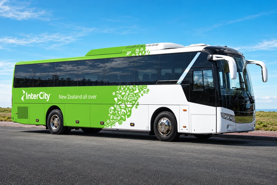 A green and white two-axle InterCity coach with dark windows and a diagonal band of New Zealand nature motifs.