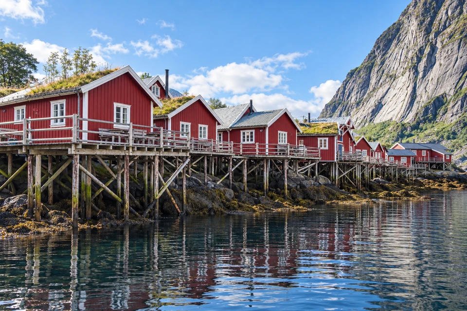 Red rorbu cabins on cross-braced timber stilts above the rocky shore at Reine in Lofoten.