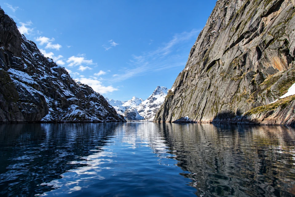 The narrow water channel of Trollfjorden between steep granite walls and distant snow-streaked peaks.