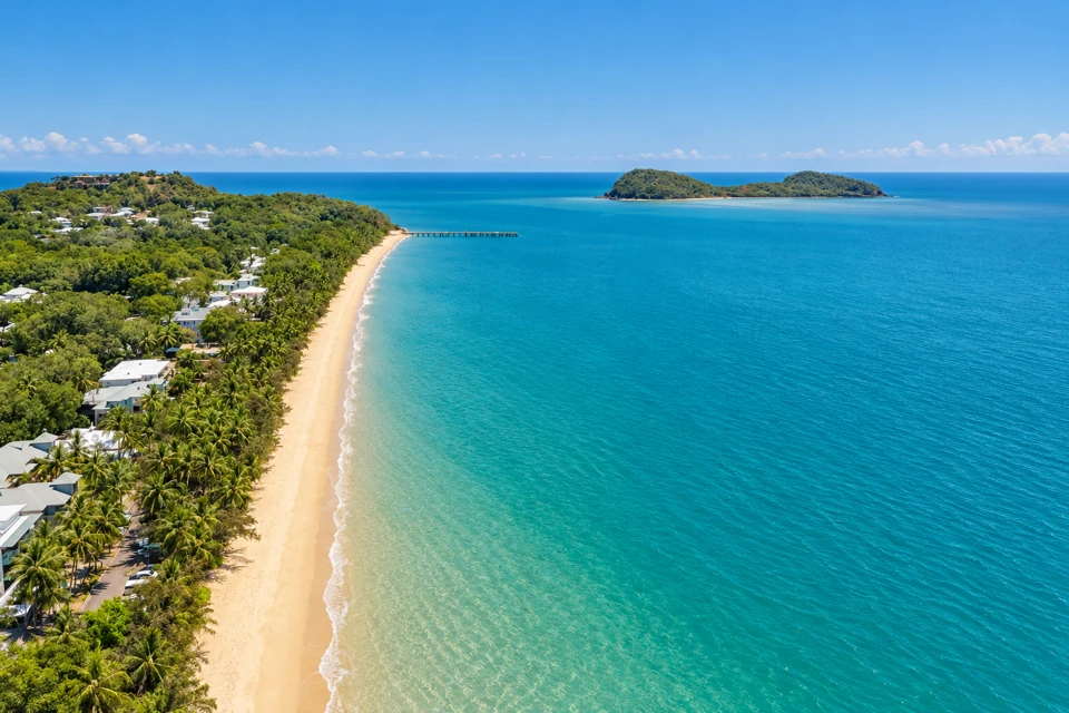 Palm-lined golden sand at Palm Cove with its jetty and low twin hills of Double Island offshore.