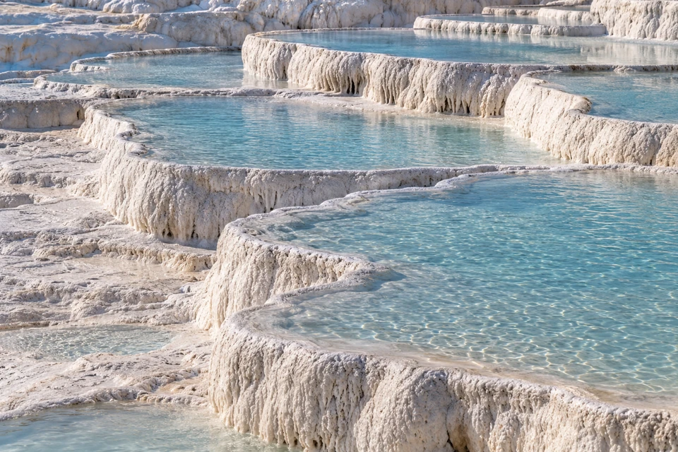 Pamukkale's shallow blue-green pools edged by thick, curved white travertine mineral rims and dry pale ridges.