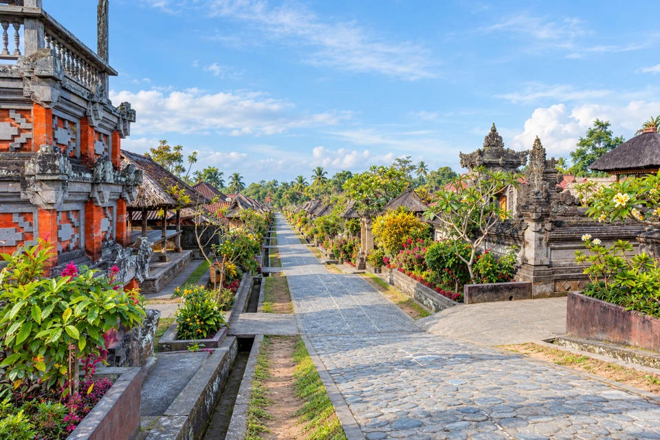 A stone lane runs between carved household gates, thatched pavilions and gardens in Penglipuran.