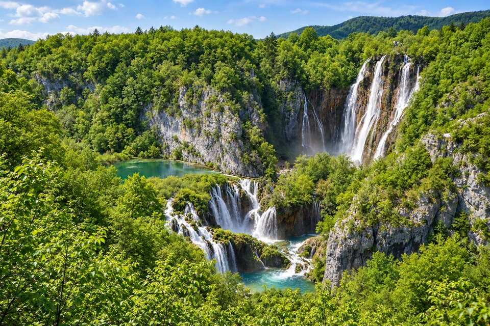 Sastavci cascades spill below a green pool at Plitvice Lakes, with tall Veliki Slap against the limestone cliff behind.