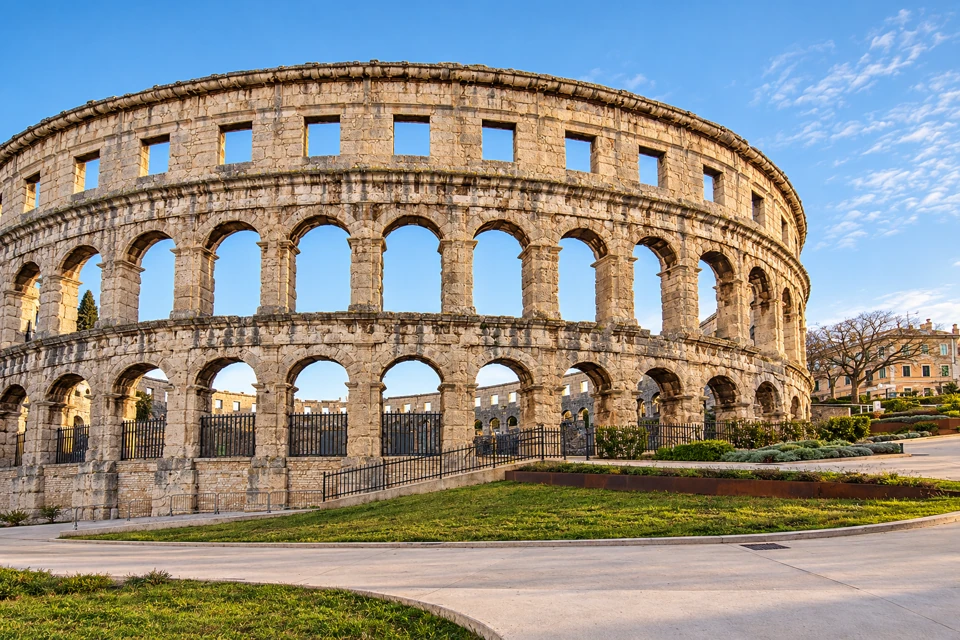 Pula Arena's curved limestone wall has two levels of rounded arches below a band of rectangular upper windows.