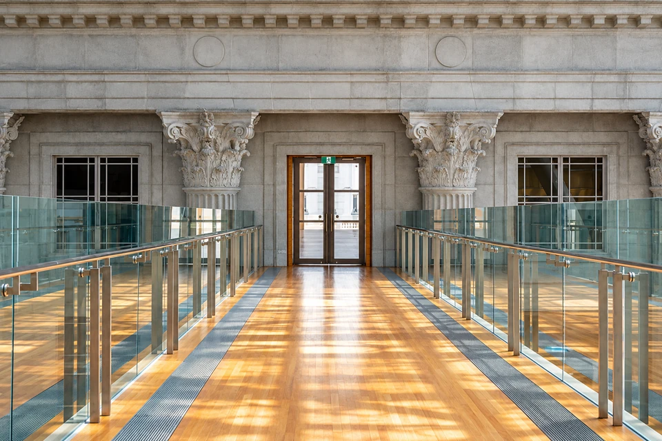 A timber and glass internal link bridge facing the carved stone City Hall Wing at National Gallery Singapore.