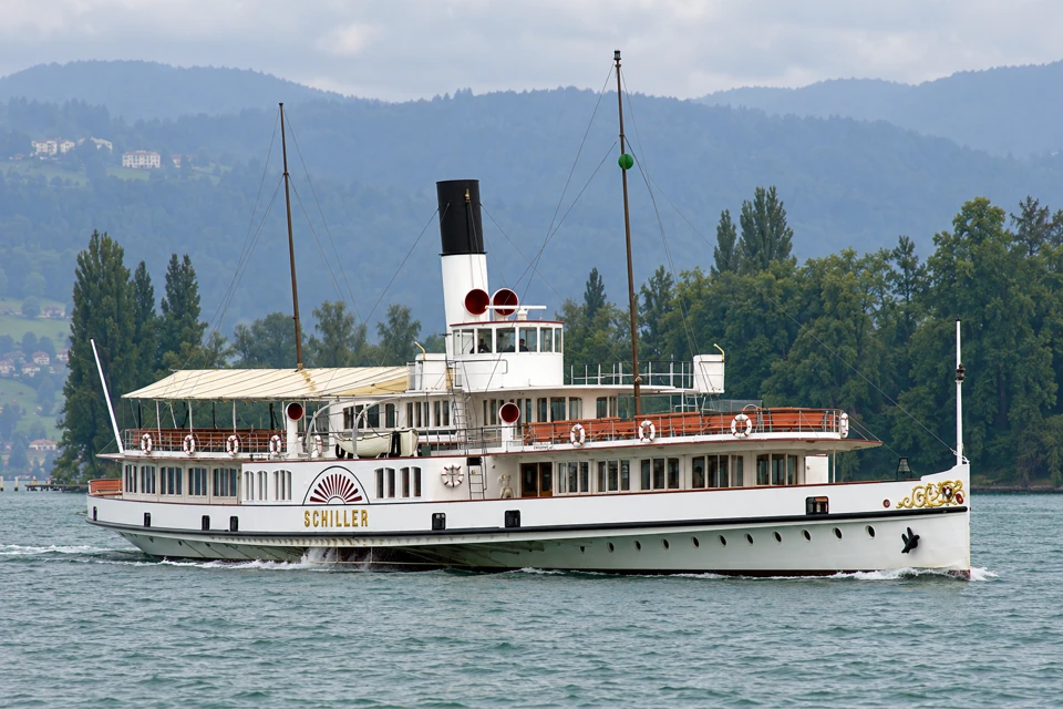 White paddle steamer Schiller on Lake Lucerne, with a black-and-white funnel, gold name and central paddle-wheel housing.