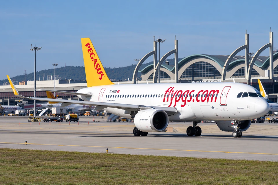 Pegasus Airbus A320neo with a yellow tail taxiing in front of Sabiha Gokcen Airport's curved green-gray terminal roof.