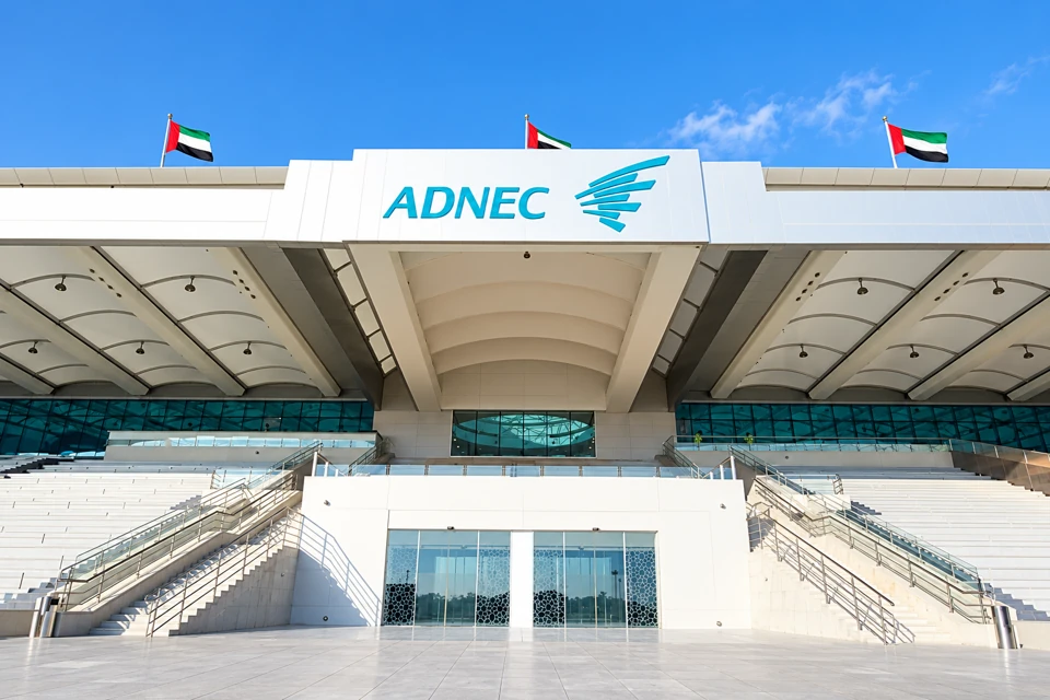 ADNEC Centre Abu Dhabi's broad white entrance canopy, turquoise identity and symmetrical stairs.