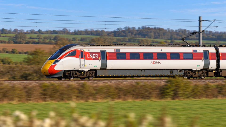 An LNER Azuma intercity train with a yellow nose, white body and red window band in the British countryside.