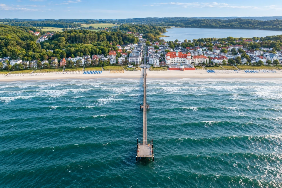 Binz's long narrow pier extending from Rugen's sandy beach, with white resort buildings and wooded hills behind.